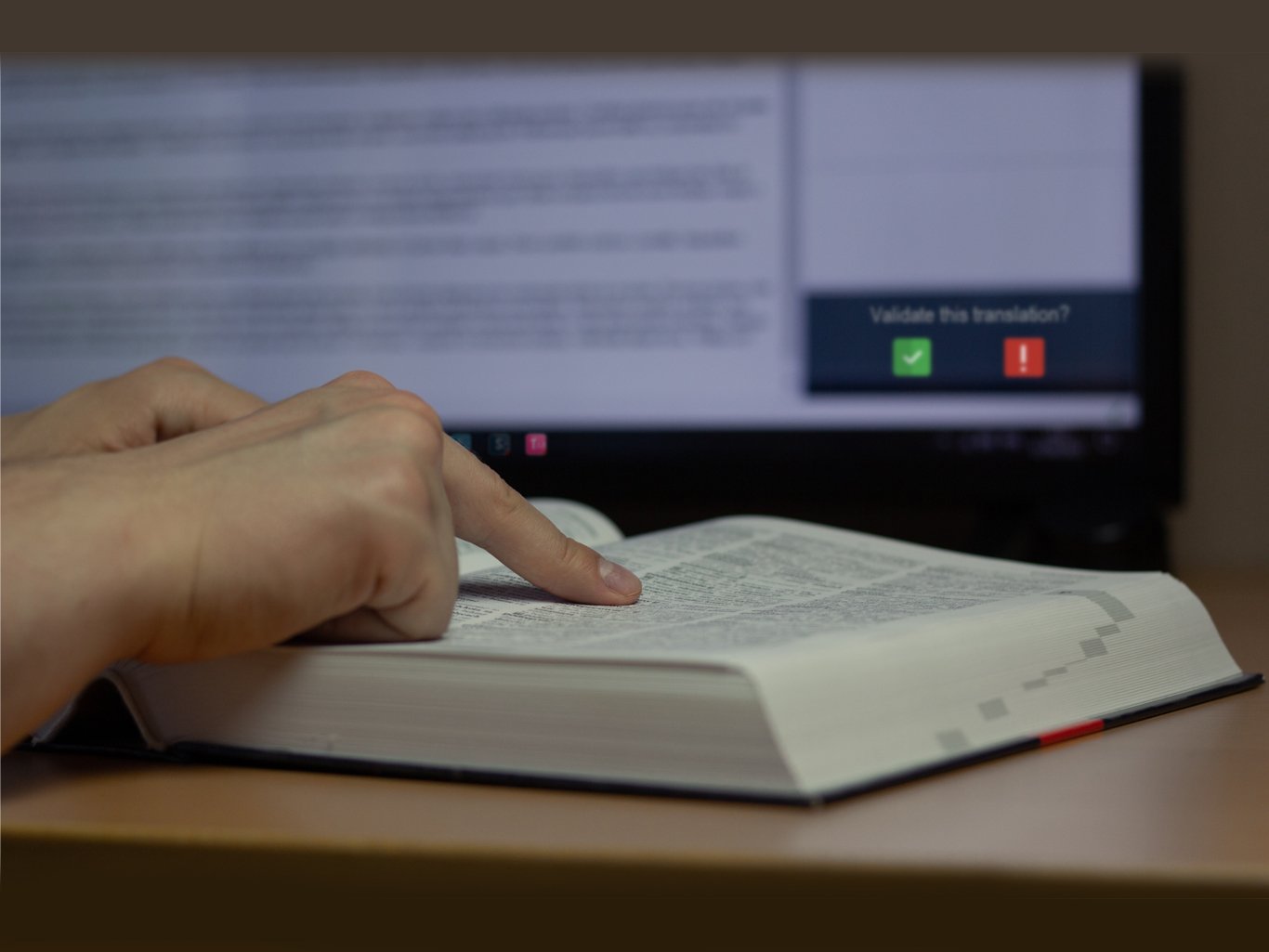 Dettaglio di un dizionario tecnico con schermo sullo sfondo che mostra l'interfaccia di validazione traduzioni.